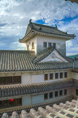 Naklejka premium Himeji, Japan - Sep 24 2024, vertical, panoramic view from window of roofs and towers with roof tiles in courtyard of Himeji Castle, White Heron Castle, at daytime with cloudy sky, Himeji, Japan