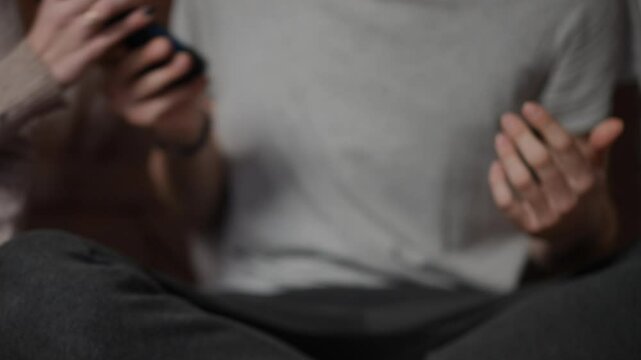 An abusive wife grabs her husband's phone from his hand while he tries to stop her. His hand is raised, showing frustration, while her grip on the phone tightens. The scene takes place indoors, with a