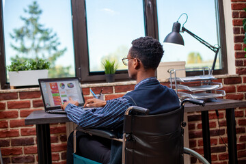 African american manager reading through strategy documents on laptop at office desk. Businessman...