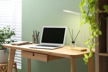 Home office. Comfortable workplace with laptop and stationery on wooden desk in room