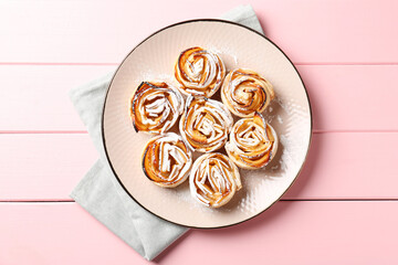 Tasty apple roses with powdered sugar on pink wooden table, top view