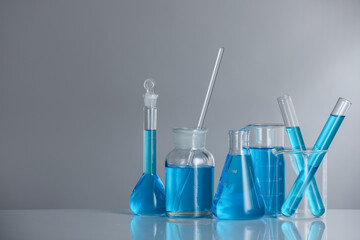 Laboratory glassware with blue liquid on mirror surface against grey background. Space for text