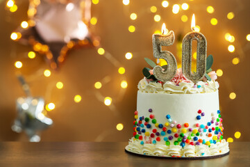 50th birthday. Tasty cake with burning number shaped candles and sprinkles on wooden table against blurred background with lights, space for text. Bokeh effect