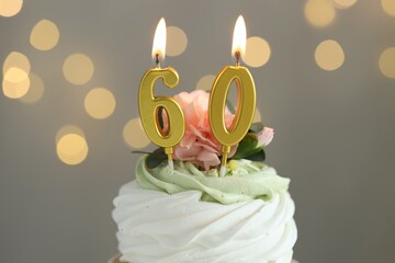 60th birthday. Tasty cupcake with burning number shaped candles on grey background with blurred lights, closeup. Bokeh effect