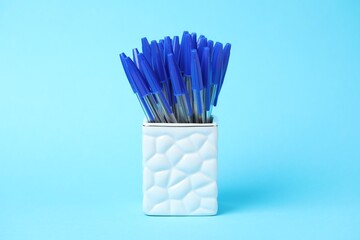 Many ballpoint pens in holder on light blue background
