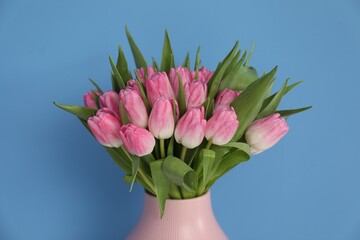 Bouquet of beautiful tulips in vase on light blue background, closeup
