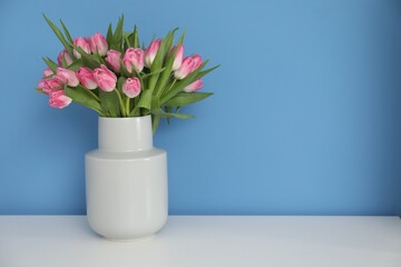 Bouquet of beautiful tulips in vase on white table against light blue background, space for text