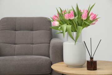 Bouquet of beautiful tulips in vase and reed diffuser on wooden table indoors, space for text