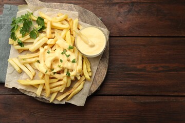 Delicious cheese sauce in bowl, French fries and parsley on wooden table, top view. Space for text