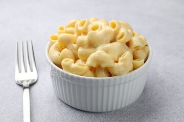 Delicious pasta with cheese sauce in bowl and fork on grey table, closeup
