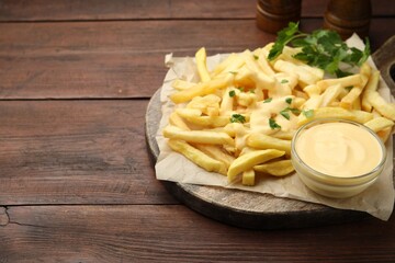 Delicious cheese sauce in bowl, French fries and parsley on wooden table, closeup. Space for text