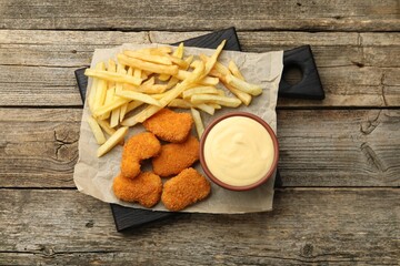 Delicious cheese sauce in bowl, chicken nuggets and French fries on wooden table, top view