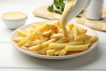 Pouring delicious cheese sauce onto French fries at wooden table, closeup