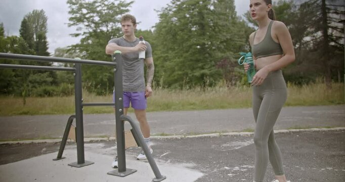 Three friends take a break from their workout in the park. They drink water and chat while catching their breath.