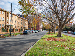 A typical North Melbourne streetscape in Australia during autumn, featuring a wide median nature...