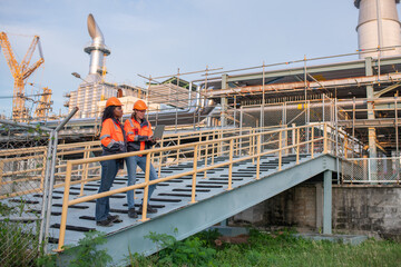 Naklejka premium Engineers wearing safety gear, including hard hats examining survey a large blueprint tablet standing industrial facility gas or oil refinery engaged in a job requires high safety standards concept.