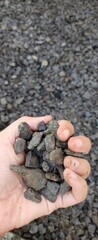 A hand holding a collection of dark grey gravel stones