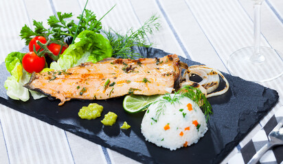 Picture of tasty fried trout fillet with rice, tomatoes and greens on black plate