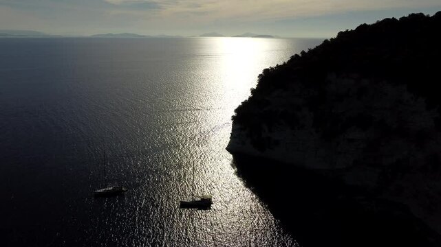 Drone shot of the sailing boats anchored off the Foki Beach in Fiskardo, Kefalonia, Greece at sunset