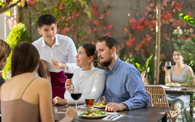 Young waiter talking to restaurant guests - taking orders for food and drinks