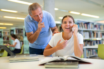 Obraz premium Elderly librarian asks young woman who is talking loudly on a mobile phone to keep quiet