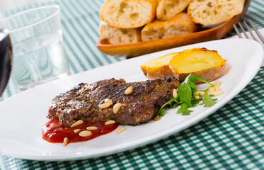 Spicy well done roasted veal steak served with baked potato, ketchup, pine nuts and greens