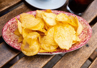 Closeup of pile of crispy potato chips on plate served with glasse of fortified red vermouth...