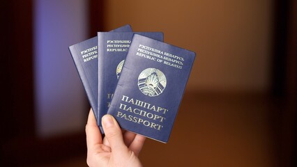 Bureaucrat holding three belarussian passports in office, processing documents for multiple individuals, evoking themes of immigration, citizenship, and international travel © treephwood