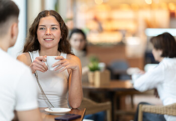 Couple of young guy and woman chatting and drinking coffee at table in cafe
