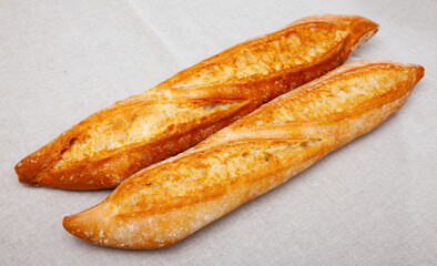 Two freshly baked French baguettes with crispy crust on fabric background