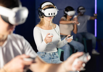 Girl in vr glasses with earbuds and two joysticks in hands is playing an active video game with...