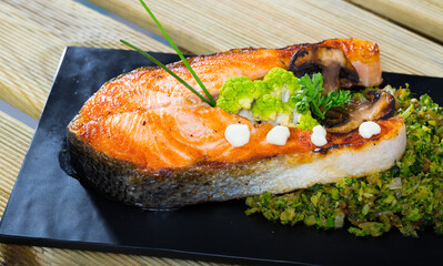 Appetizing roasted salmon steak served with broccoli, vegetables and herbs on slate