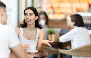 Woman at a meeting with a guy communicates with interest. European woman sitting at a table in a coffee shop and talking to a man in front of visitors