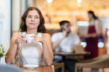 Young European woman enjoys a cup of hot quality coffee made from Arabica beans. Woman enjoys drinking cappuccino in a coffee shop