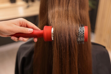 Fototapeta premium Hairdresser styling client's hair with round brush in salon, closeup