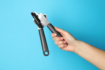 Woman holding can opener against light blue background, closeup