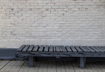 Full frame abstract texture background of a blueish gray wooden bench along a grungy white painted brick wall that shows wear and peeling paint.
