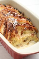 Freshly baked bread pudding in baking dish on white wooden table, closeup
