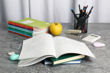 Doing homework. Notebook with math assignment, apple and stationery on grey desk
