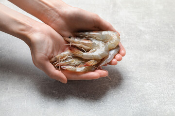 Woman with fresh raw shrimps at grey table, closeup. Space for text