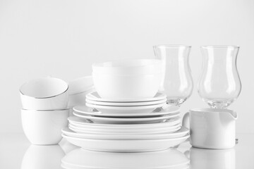 Different clean dishware and glasses on light background