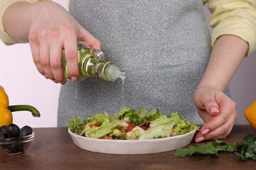 Woman pouring oil onto tasty salad at wooden table against white background, closeup