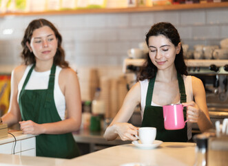 Young woman barista pouring freshly brewed coffee into cup in cafe