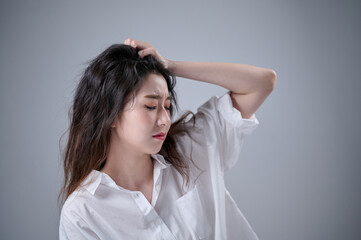 Naklejka premium A young woman with disheveled long hair holds her head with both hands, looking troubled.