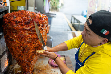 Street vendor slicing meat from a rotating spit to prepare tacos al pastor at a traditional mexican...