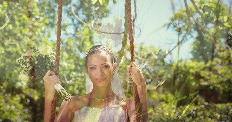 Bride holding bouquet on swing in garden, enjoying sunny wedding day