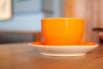 Bright orange cup and saucer on wooden table in cozy cafe setting