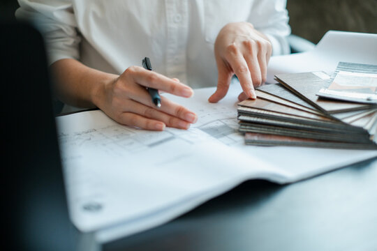 Designer examining material samples and blueprints at a desk, showcasing creativity and attention to detail in interior design.
