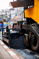 asphalt paving machine lays fresh blacktop on a city street , with steam rising from the hot surface and a construction worker visible in the background.