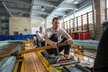 Exhausted determined rowers push limits training intensely on rowing simulator in gym pool. Male...